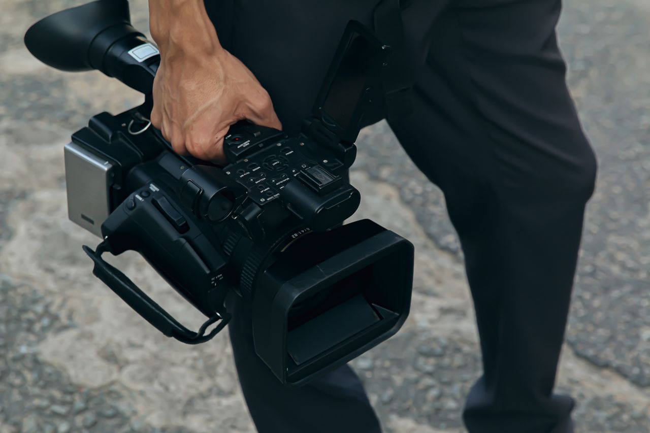 A detailed view of a person carrying a professional video camera outdoors.