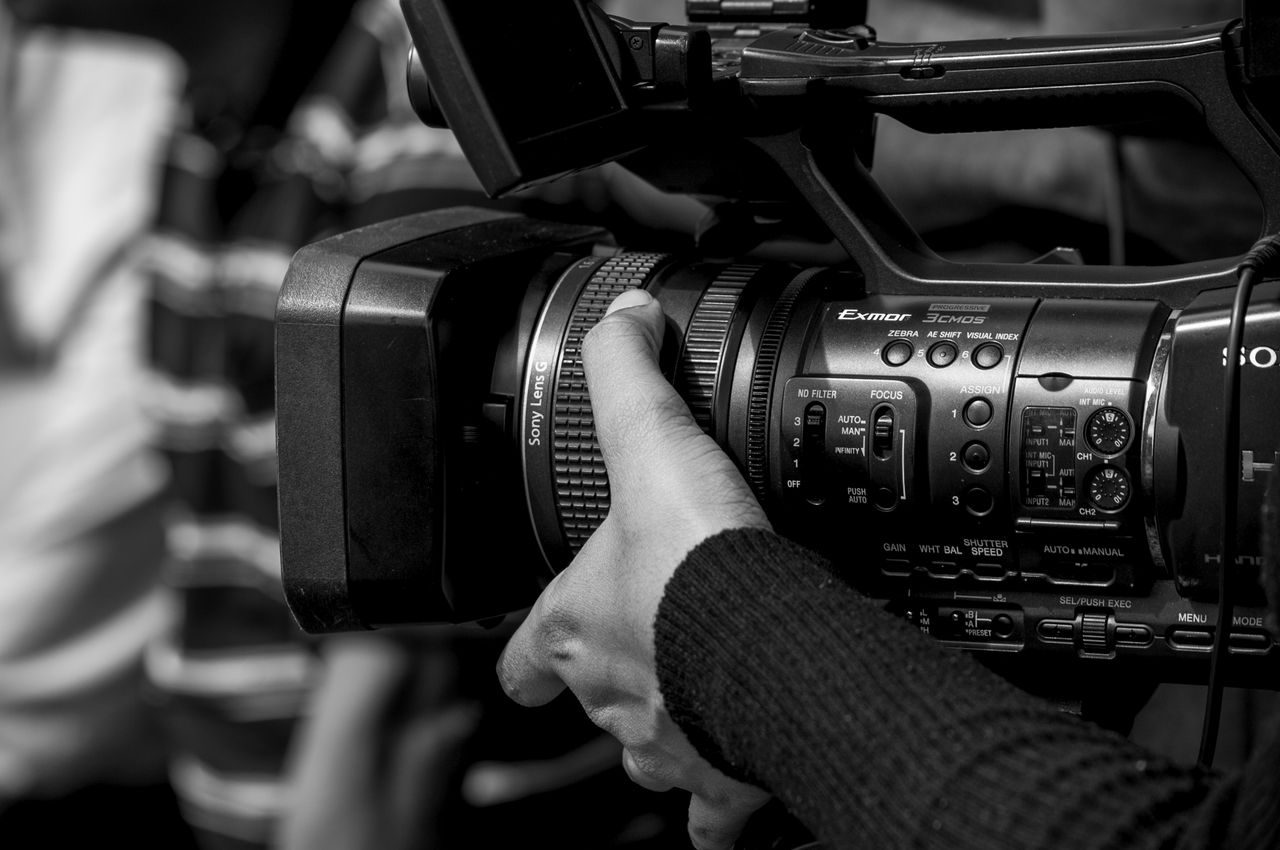 Black and white image of a person operating a professional video camera, showcasing detailed camera controls.