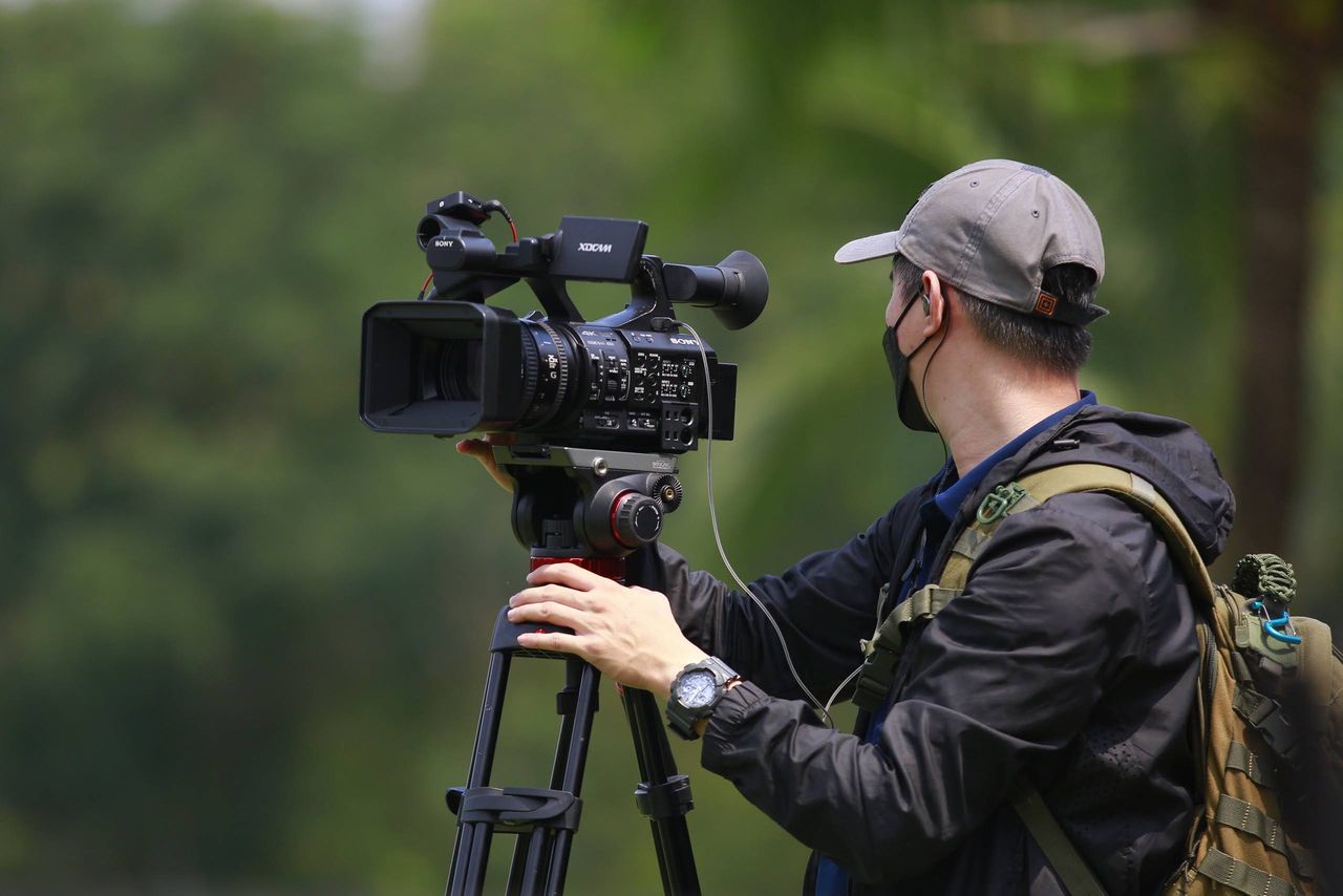 Cinematographer in action outdoors, adjusting a professional video camera on a tripod.