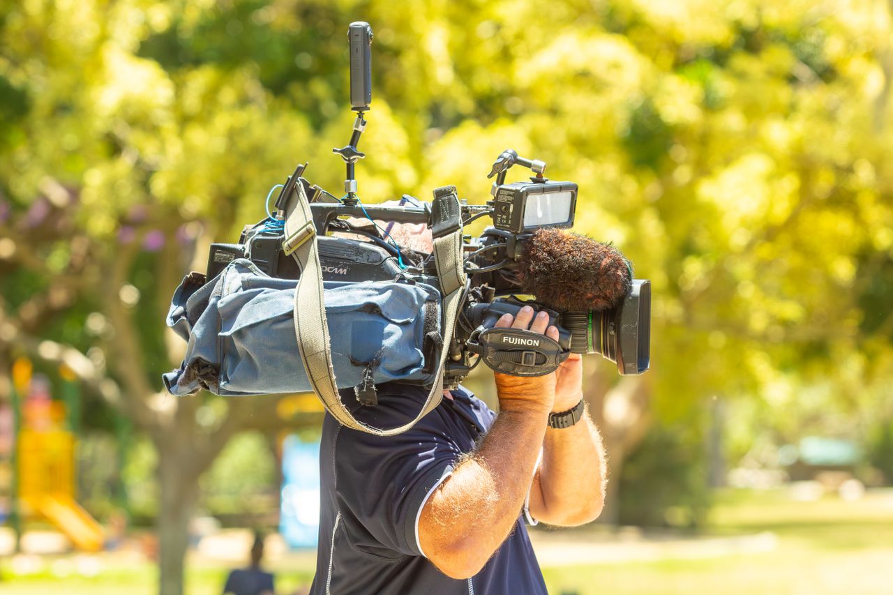 Outdoor filming scene with a cameraman operating professional equipment in a sunny park.